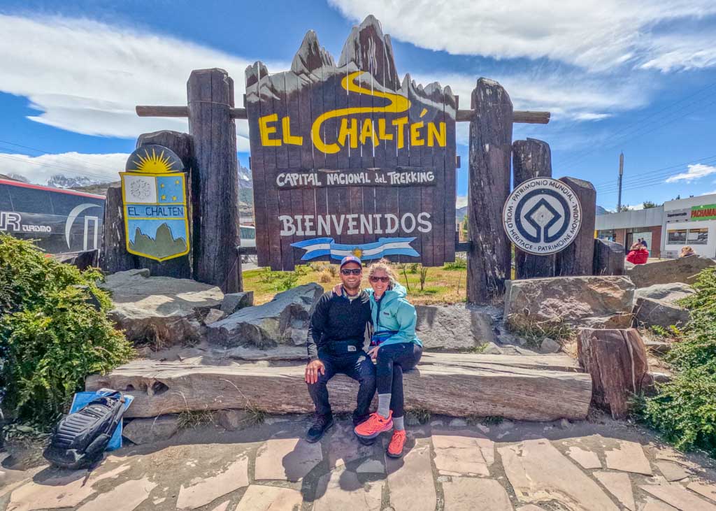 Two people sitting in front of a sign before going trekking in El Chalten