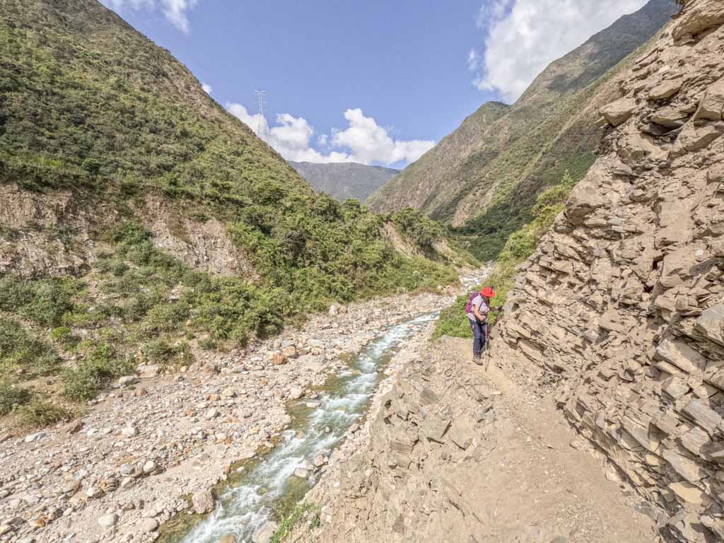 A woman walking on the side of a mountain with a river beneath her