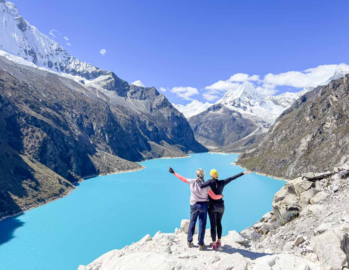 two people standing with their hands in the air at Laguna Paron in Huaraz, Peru
