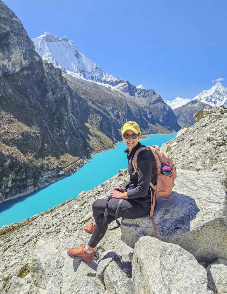 A woman sitting on a rock with a blue lake behind her