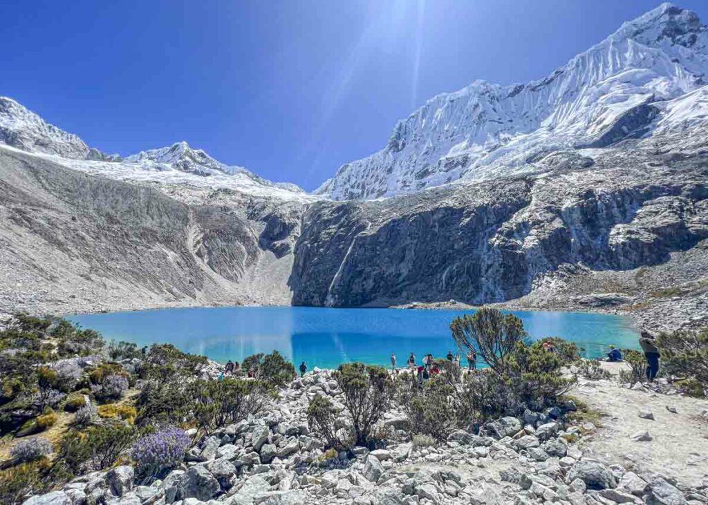 A person walking to a blue lake surrounded by mountains after the laguna 69 hike