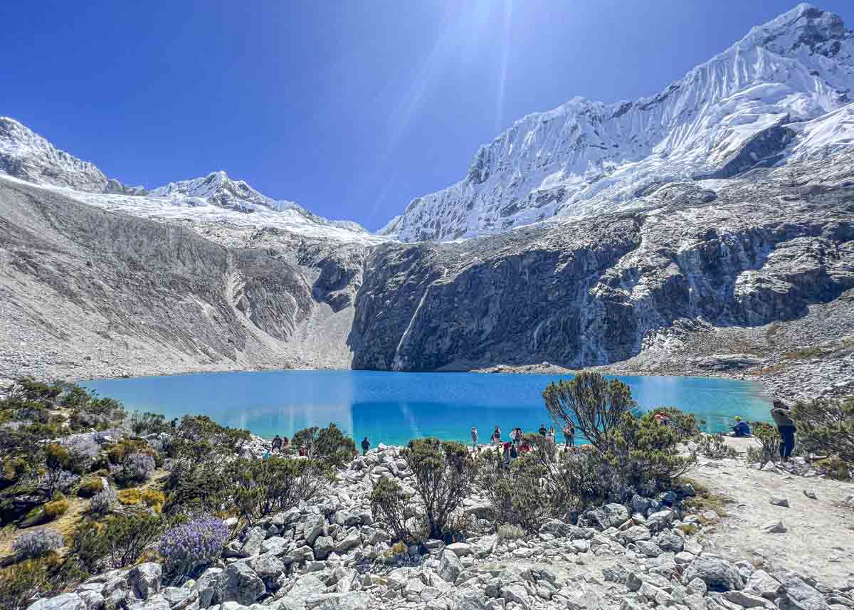 A person walking to a blue lake surrounded by mountains after the laguna 69 hike